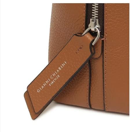 Cận cảnh chiếc túi da màu nâu của GIANNI CHIARINI. Nó có khóa kéo kim loại và thẻ da có dòng chữ "GIANNI CHIARINI FIRENZE" màu trắng. Nó được sản xuất tại Ý và toát lên vẻ sang trọng vượt thời gian của Ý.
